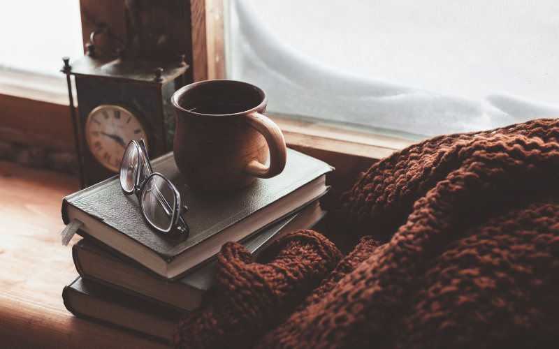 a coffee cup and black rimmed glasses stacked on a pile of books by a window