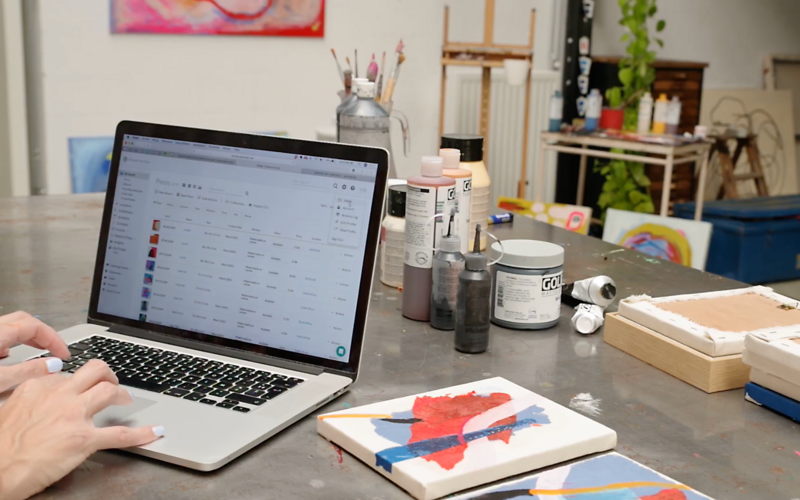 An abstract artist with Caucasian hands types on a keyboard in their art studio, logged into their Artwork Archive account on the computer.