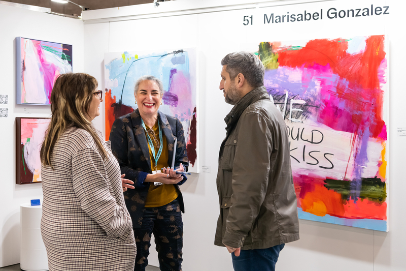 Three individuals standing in front of colorful abstract paintings smiling and talking to eachother