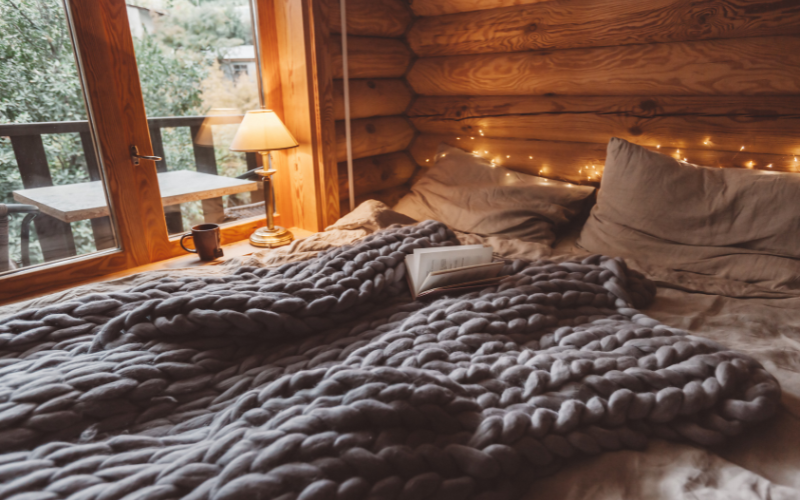 a bed with a grey throw blanket and fairylights in a log cabin 