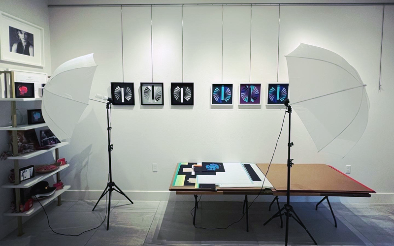 Two large photography lights shine on a wall of hanging artwork by Jessey Jansen, to be photographed by the artist. 